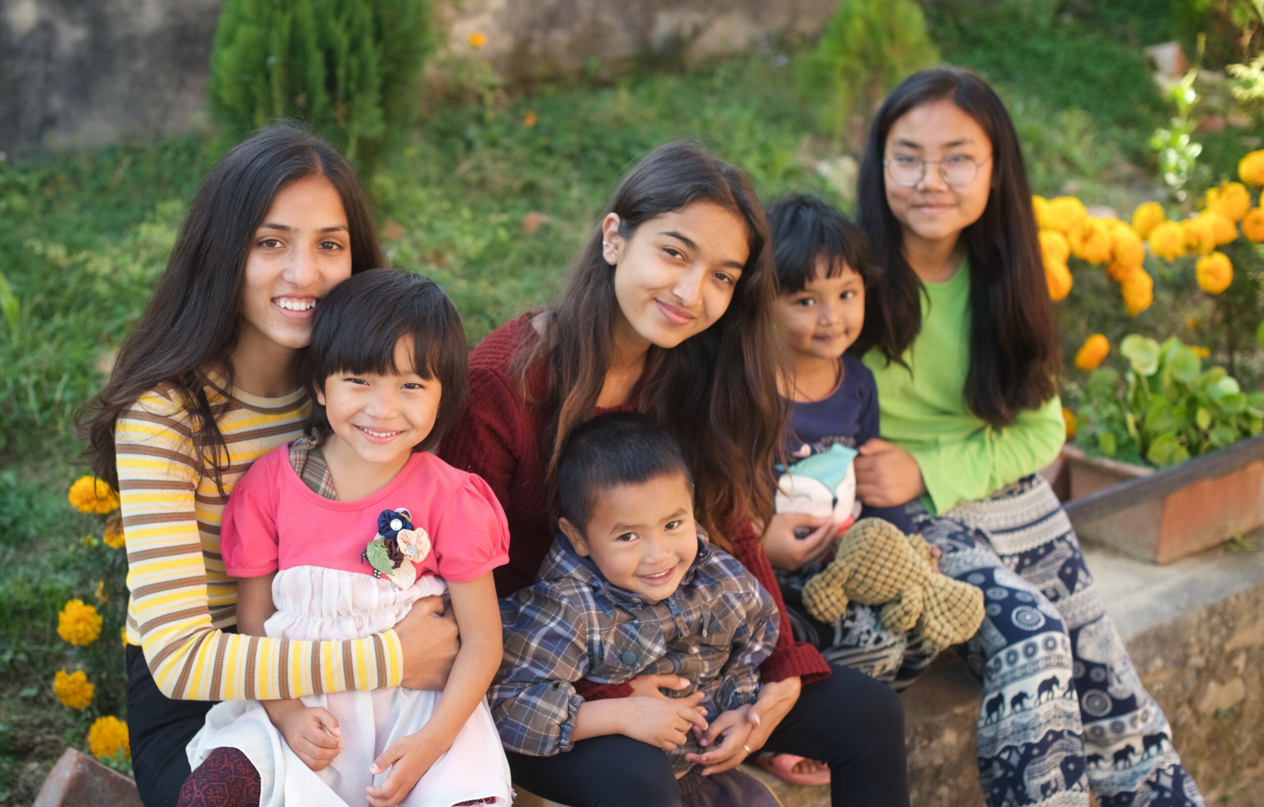 Six children, all from Olgapuri Children's Village, smile at the camera. They are hugging each other to show care, love, and gratitude.