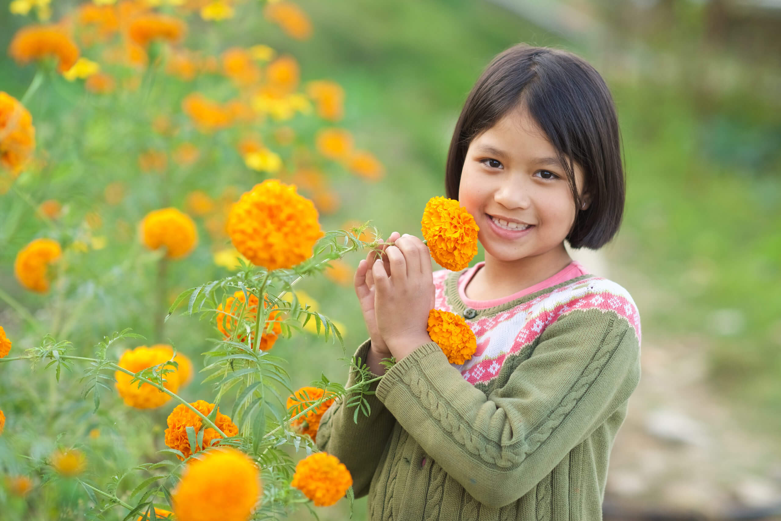 A young girl at Olgapuri Children's Village smiles as she holds flowers in a garden.