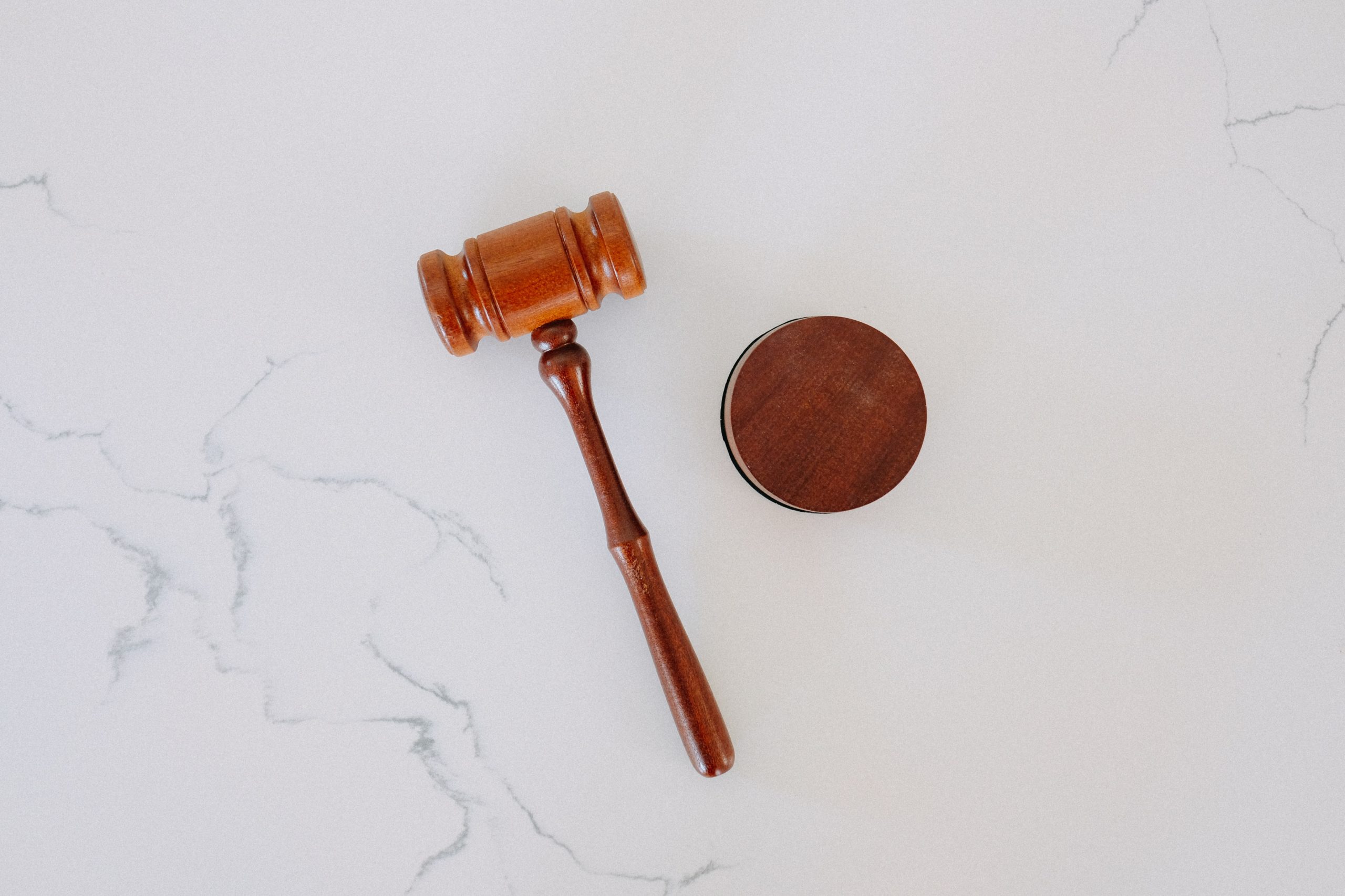 A wooden gavel is pictured from above, resting on a light grey marble surface.