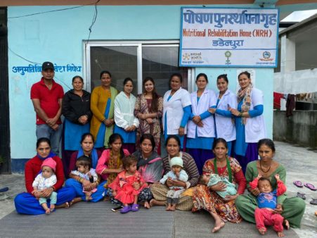 Nine Dadeldhura Nutritional Rehabilitation Home staff members stand behind their patients: a group of seven women and their small children.