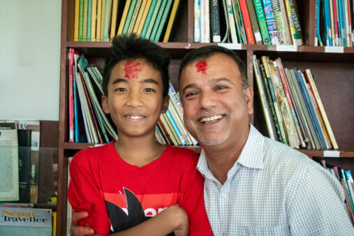 NYF President Som Paneru smiles into the camera with a junior boy at Olgapuri. They both have tika on their foreheads.