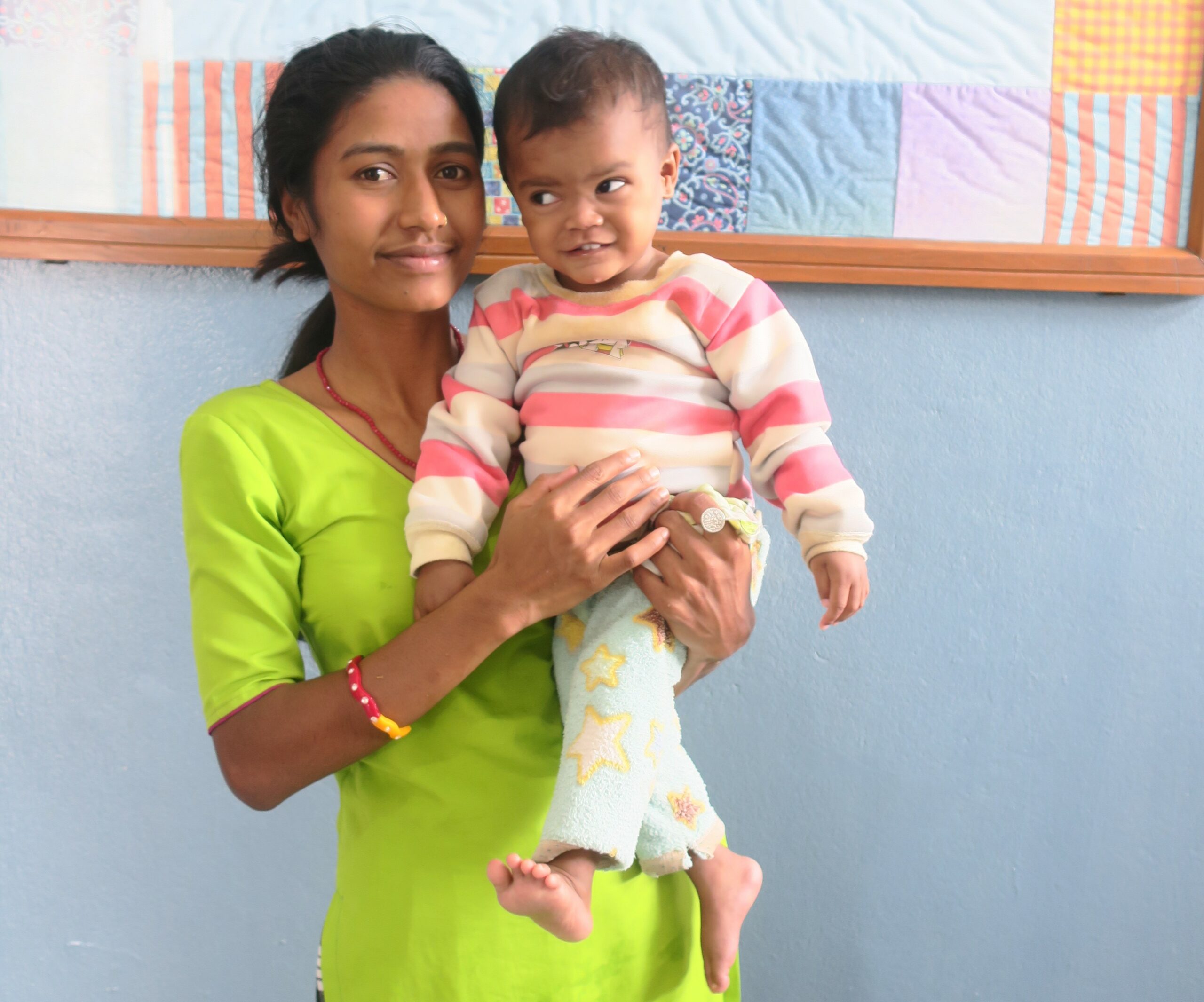 a young Nepali woman in a bright green dress holds a smiling, wiggling toddler to pose for the camera
